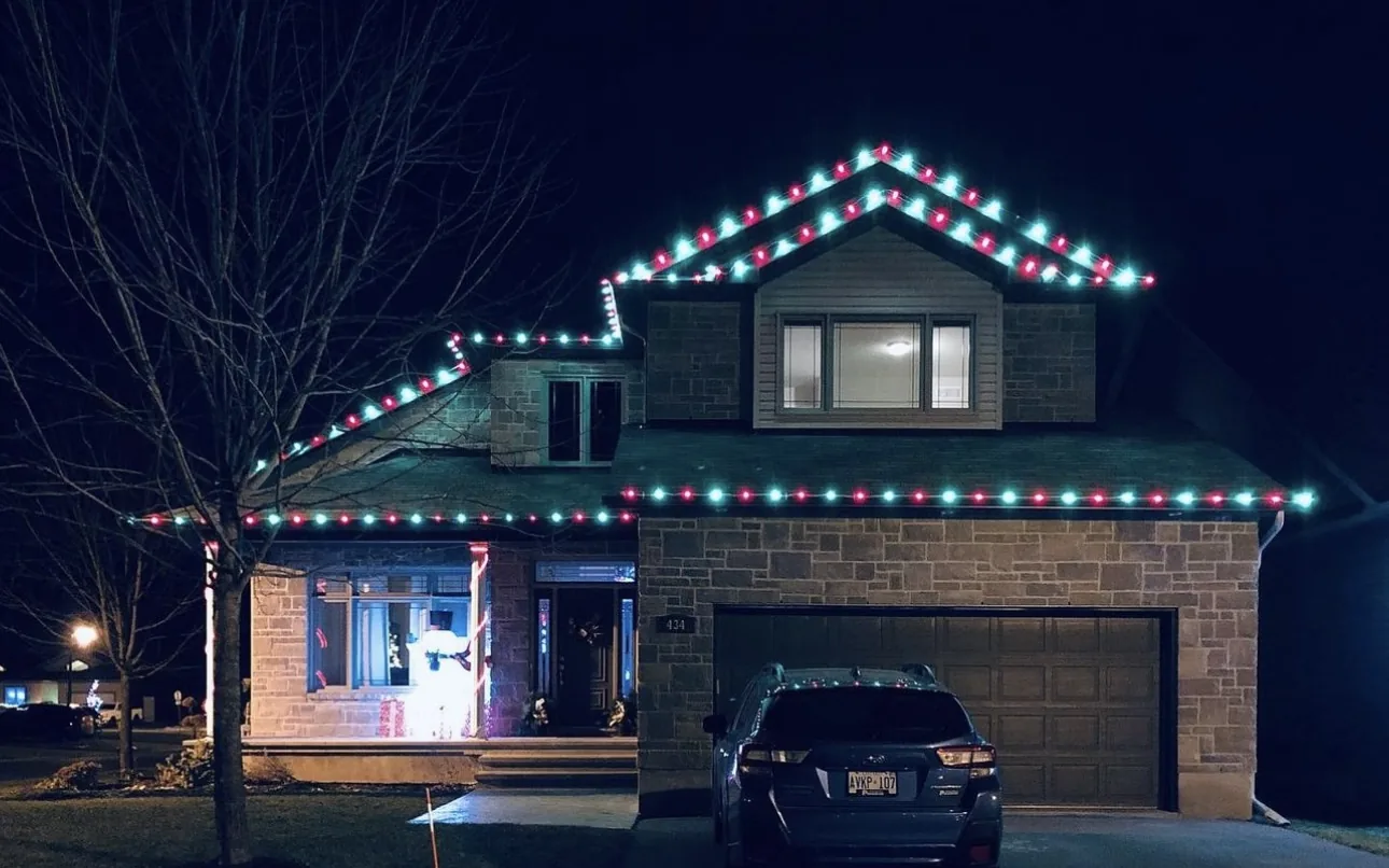 Two-story home outlined in alternating red and cool white holiday lighting